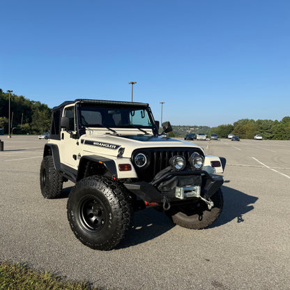 White Jeep Wrangler parked in a parking lot with trees in the background