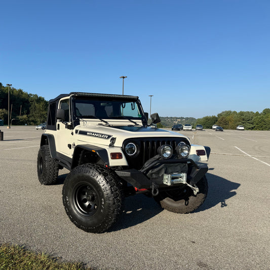 White Jeep Wrangler parked in a parking lot with trees in the background