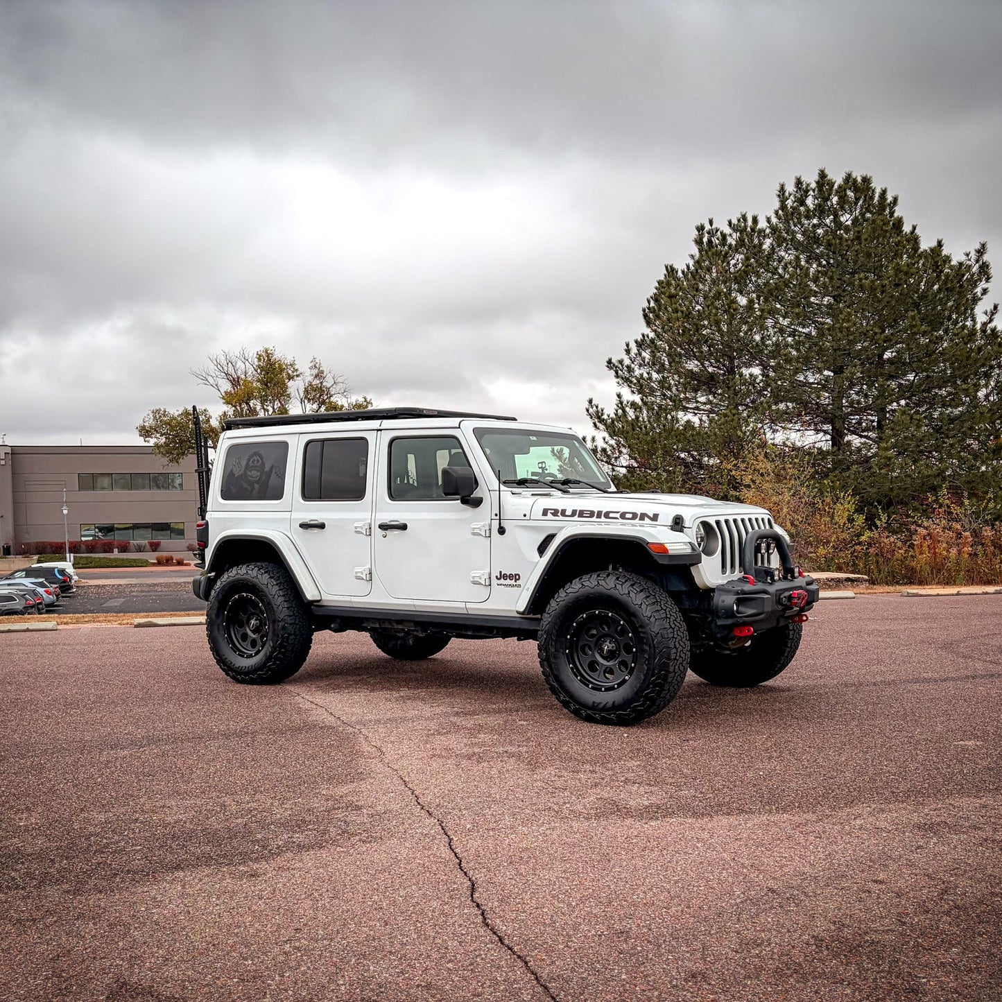 White Jeep Wrangler Rubicon parked in a lot with trees and buildings in the background