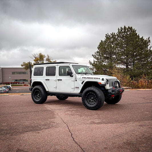 White Jeep Wrangler Rubicon parked in a lot with trees and buildings in the background